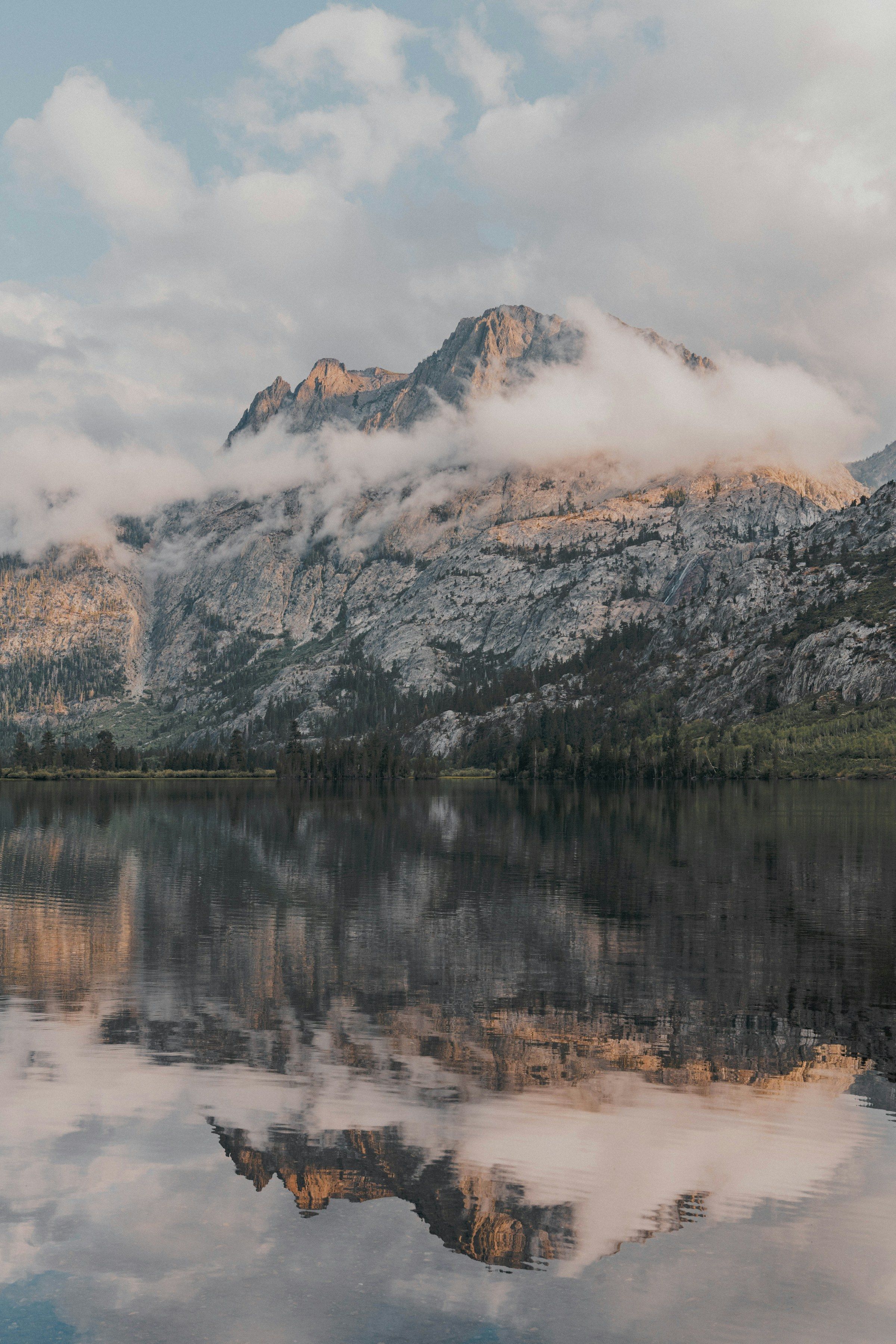 Felsige Berge mit Wolken spiegeln sich fast symmetrisch im ruhigen Wasser eines Sees