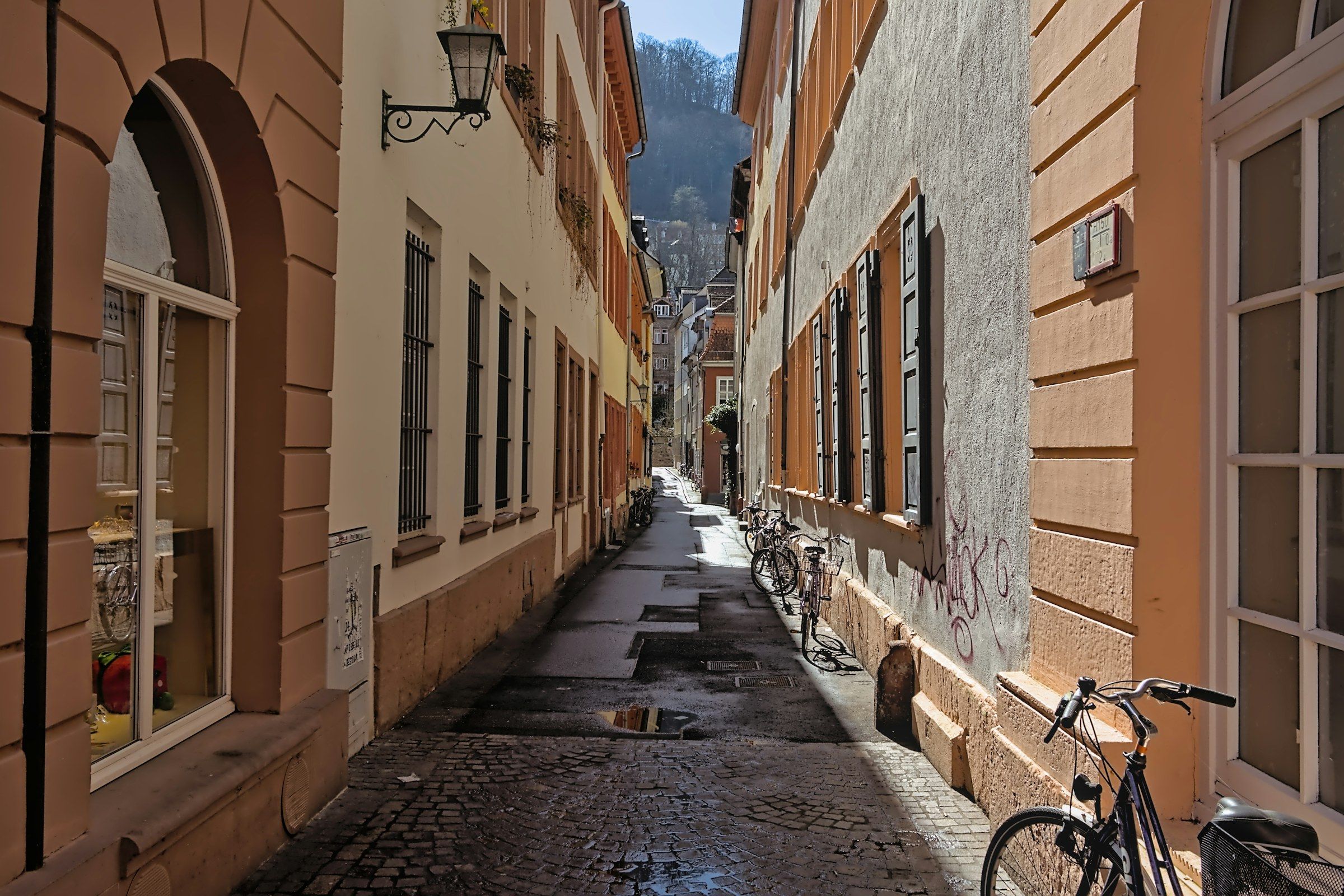 Schmale, nasse Gasse zwischen hohen Altstadthäusern mit einer Laterne und einem abgestellten Fahrrad
