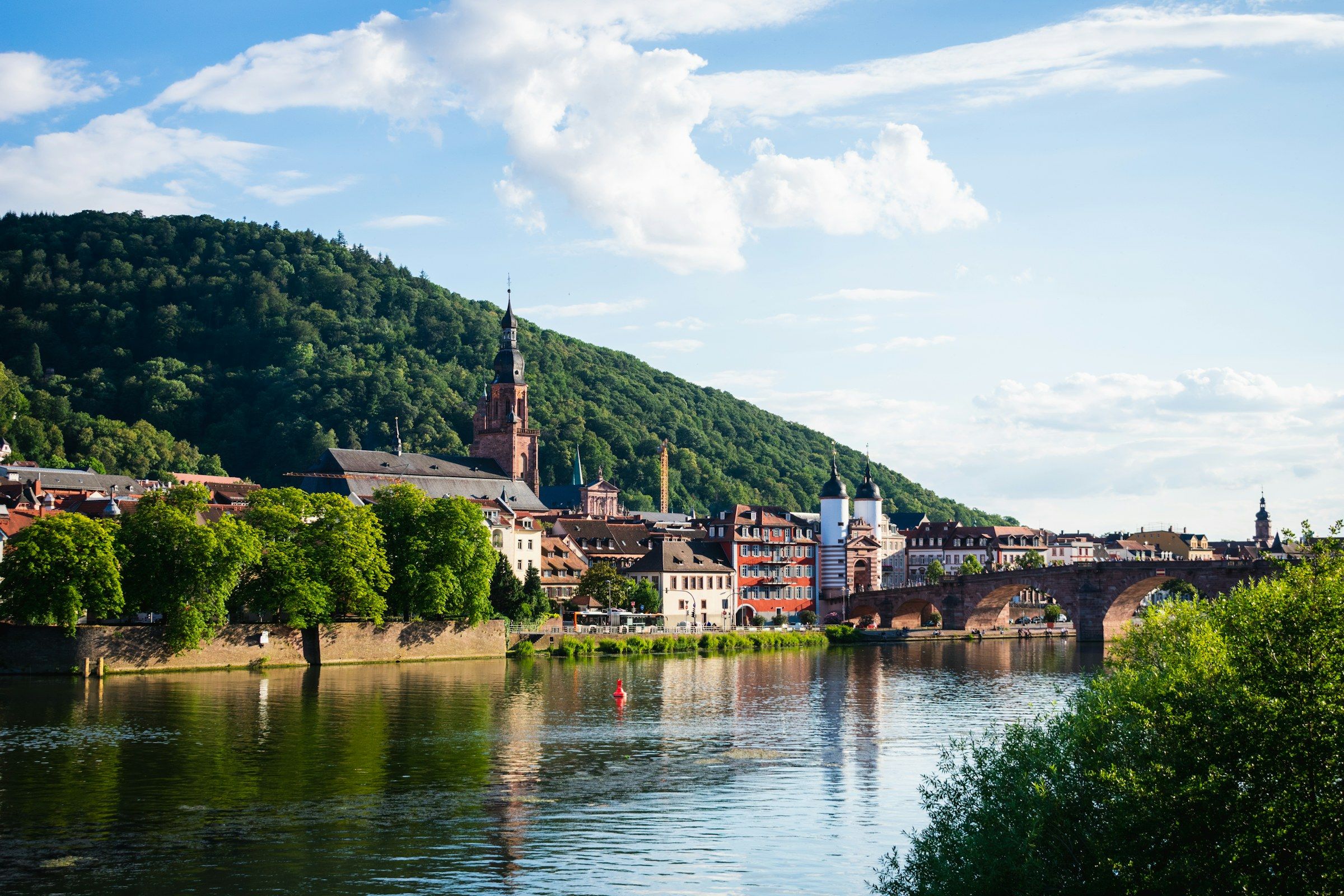 Neckarufer in Heidelberg mit Altstadthäusern, Kirchturm und Brückentor an einem sonnigen Tag