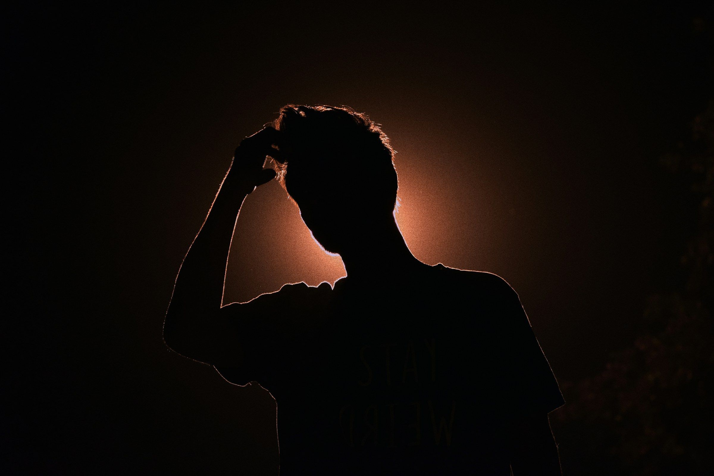 Silhouette eines Mannes vor schwach leuchtendem Hintergrund, fast das ganze Bild ist dunkel